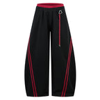 Black loose trousers with red side stripes and a red contrast waistband.