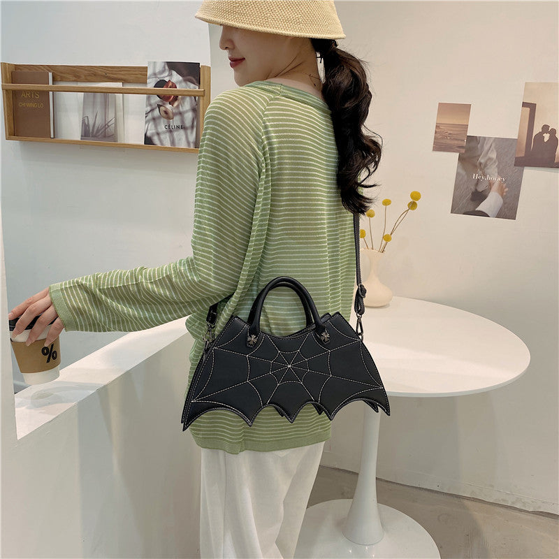 Black bat-wing-shaped bag worn at the hip with its shoulder strap over a green striped top.