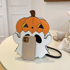 White ghost-shaped bag with an orange pumpkin hat on a table beside a phone for scale.