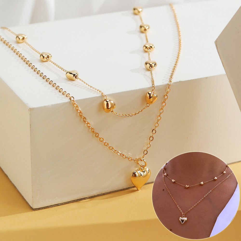 Gold-tone double-layer heart necklace displayed over a white block with a circular on-body inset.
