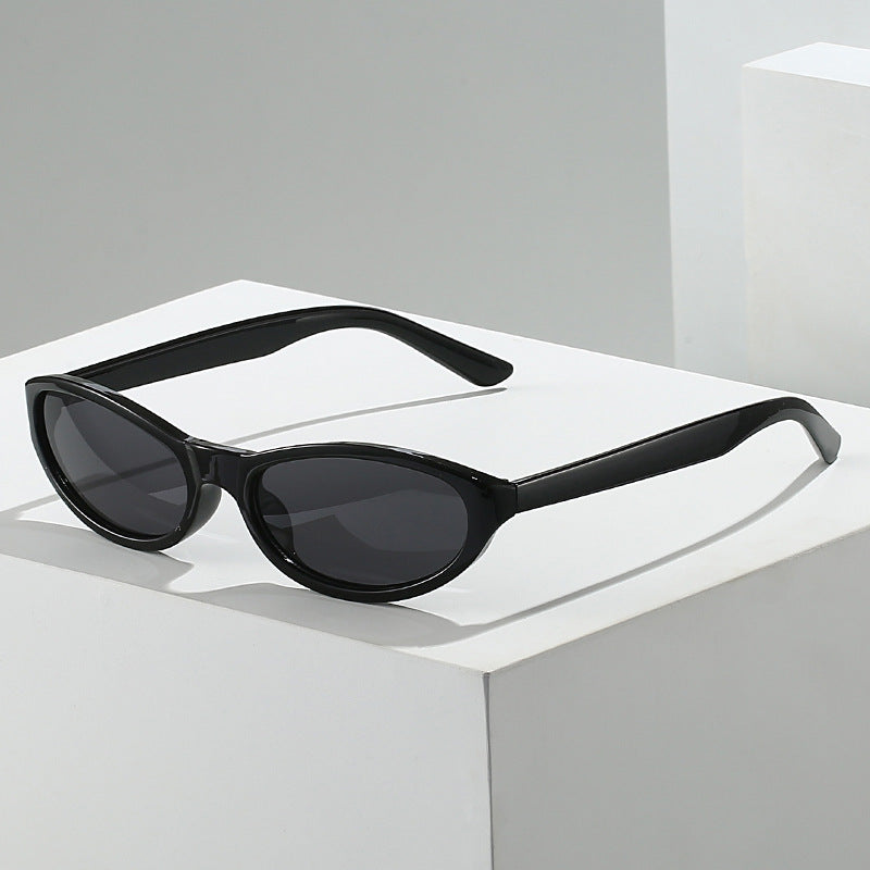Black narrow oval sunglasses displayed on a white pedestal