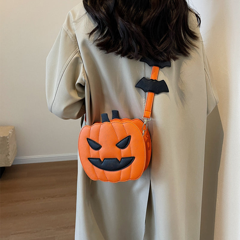 Orange jack-o’-lantern crossbody bag with black face and bat details on the strap, shown worn