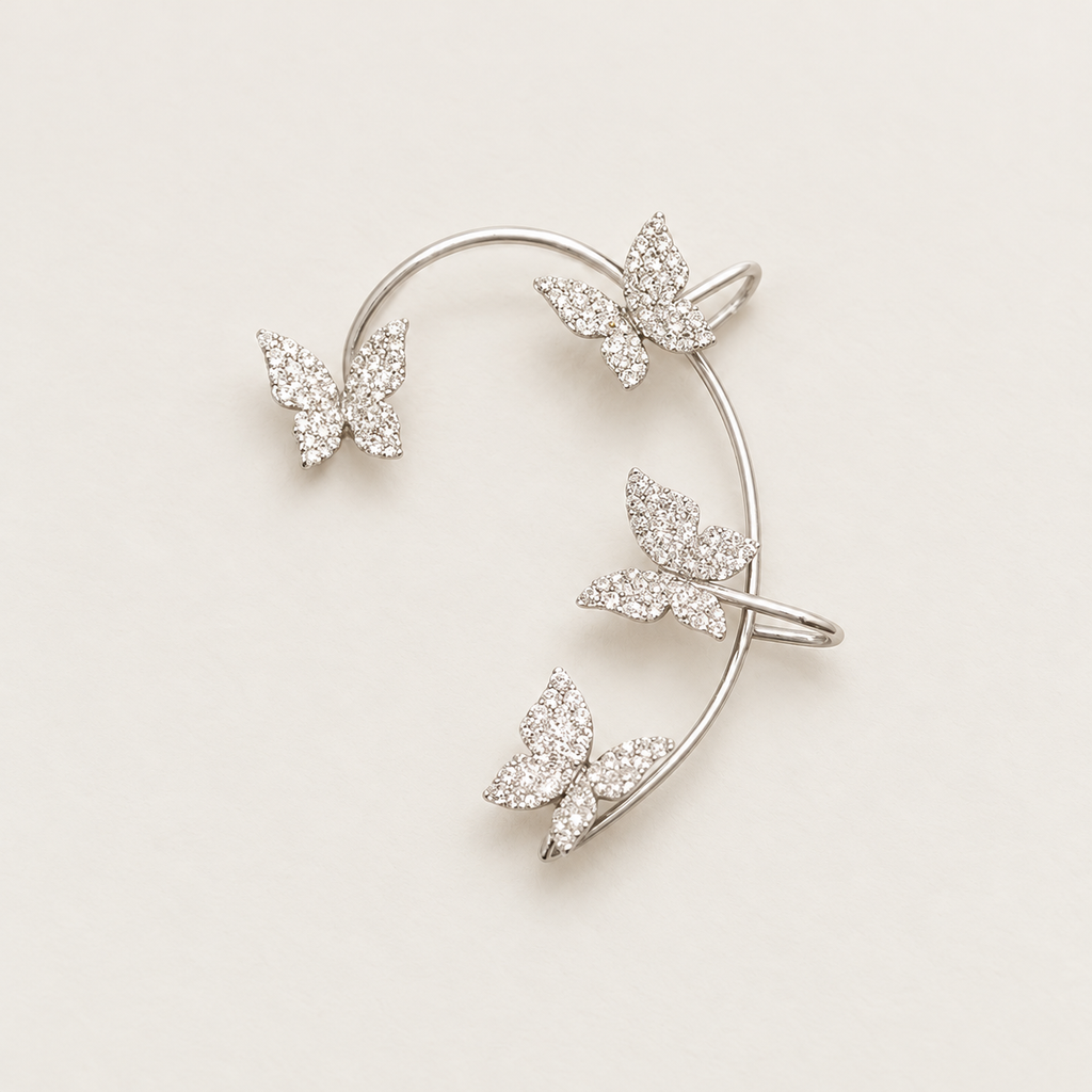Silver-tone curved ear cuff with four butterfly details on a warm ivory background