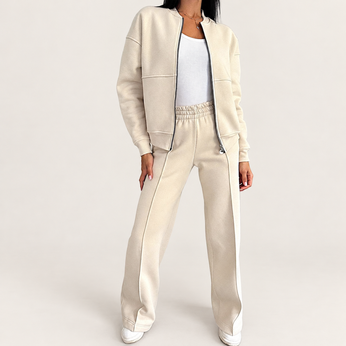 Model wearing a cream zip jacket and matching wide-leg trousers against a warm ivory studio background