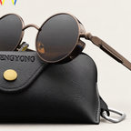 Bronze-tone round steampunk sunglasses resting on a black glasses case against a warm ivory studio background