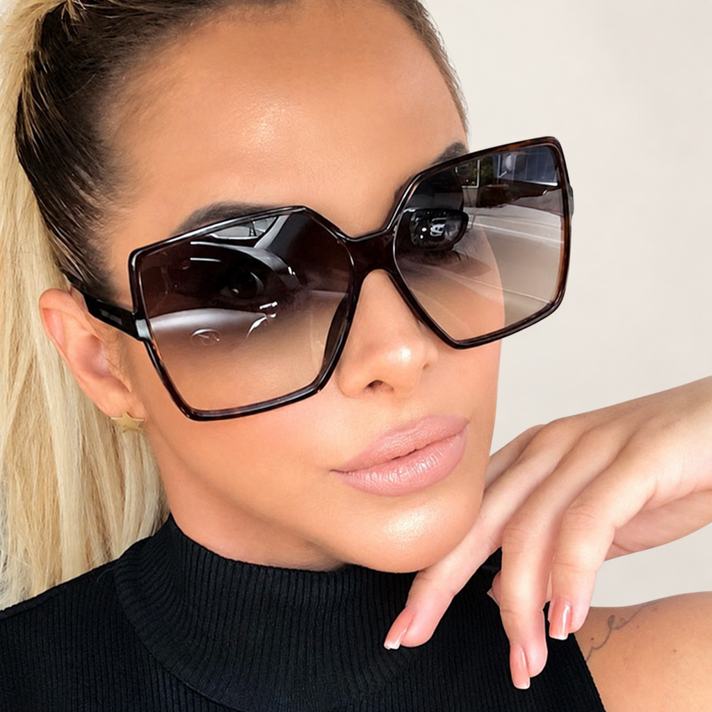 Woman wearing oversized black angular sunglasses with gradient lenses against a warm ivory studio background