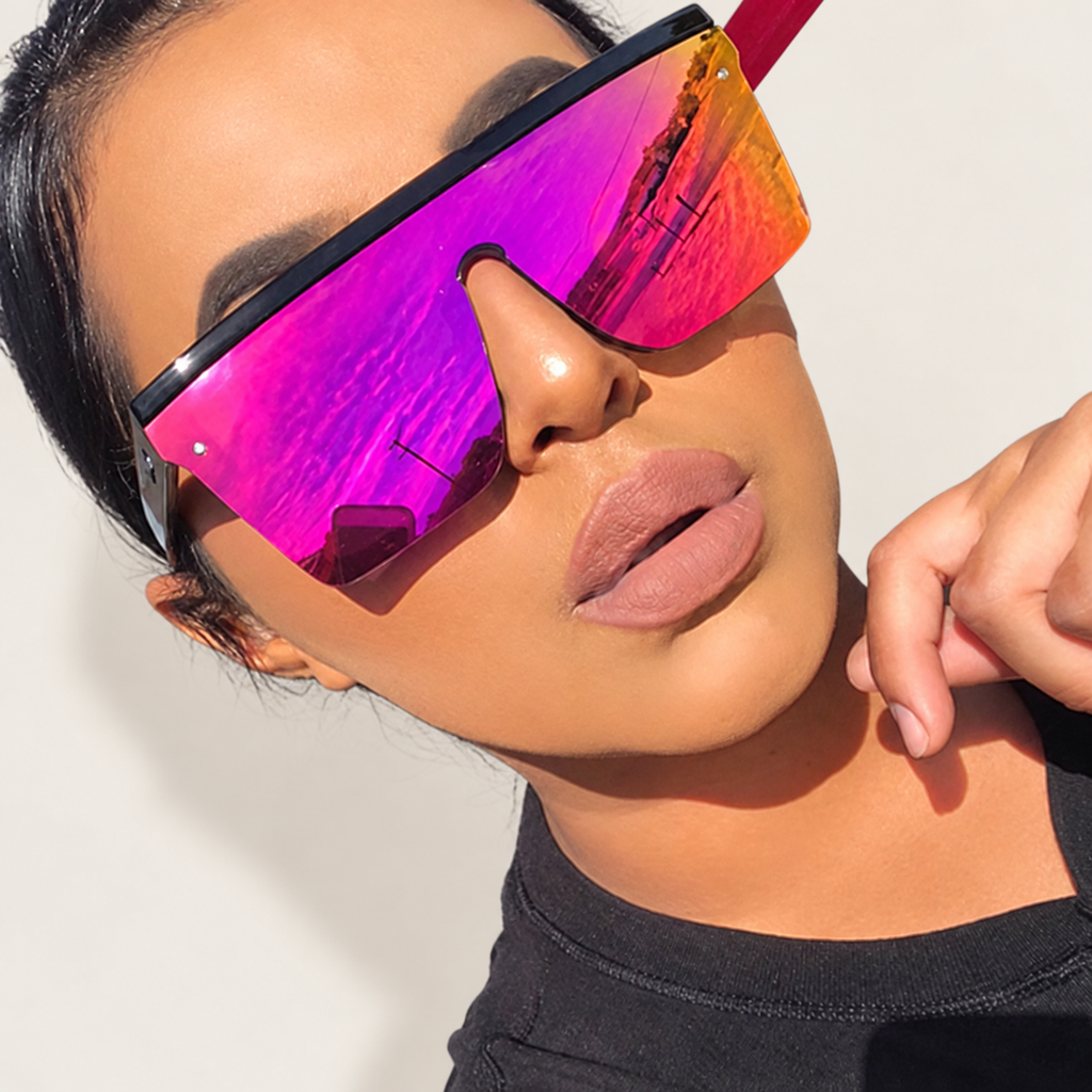 Woman wearing magenta-orange mirrored shield sunglasses against a warm ivory studio background