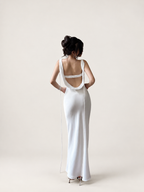 Back view of a white satin maxi dress with an open cowl back and long ties against a warm ivory studio background
