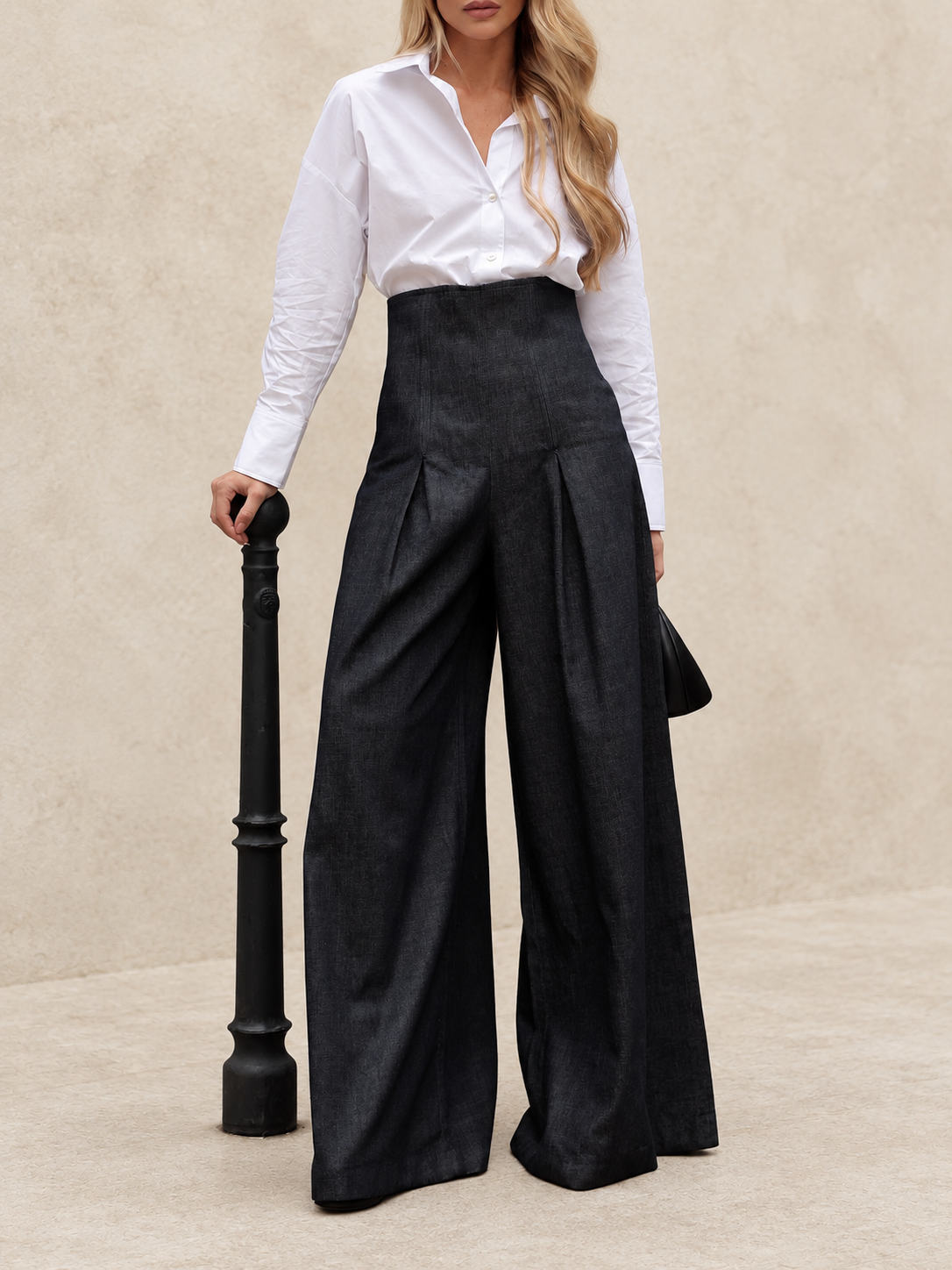 Dark charcoal high-waist pleated wide-leg trousers worn by a model against ivory
