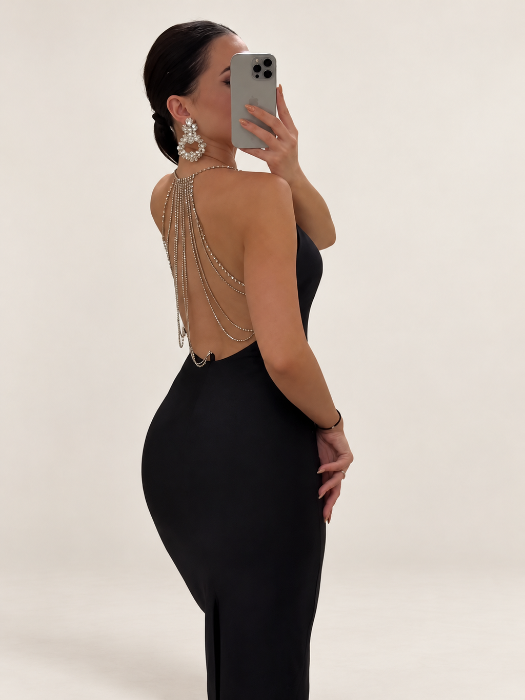 Back view of a black fitted dress with cascading rhinestone chains against a warm ivory studio background