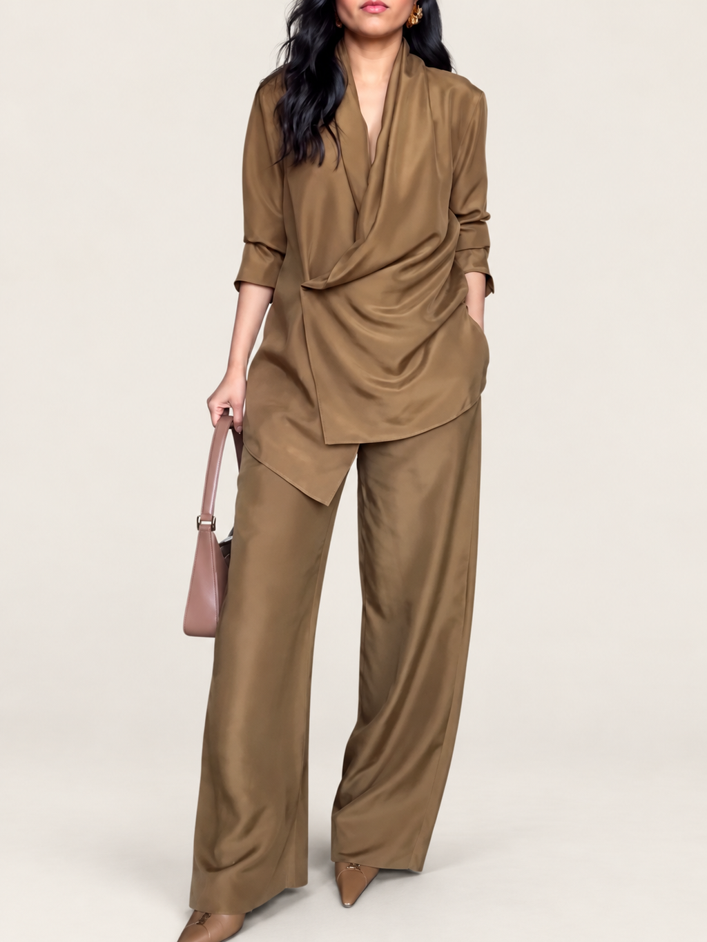 Model wearing a camel wrap blouse and wide-leg trousers against a warm ivory studio background