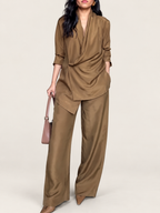 Model wearing a camel wrap blouse and wide-leg trousers against a warm ivory studio background