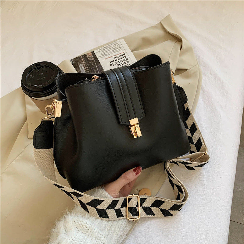 Black bucket bag with gold-tone clasp and patterned wide shoulder strap