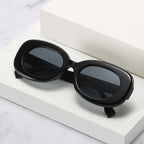Black oval sunglasses with dark lenses displayed on white stepped blocks.