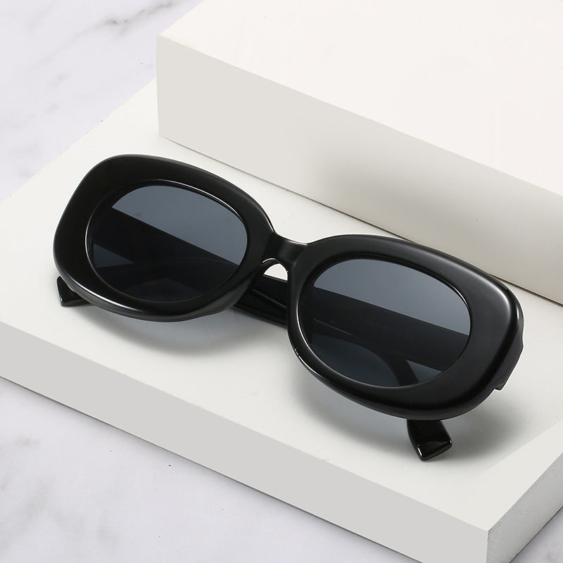 Black oval sunglasses with dark lenses displayed on white stepped blocks.