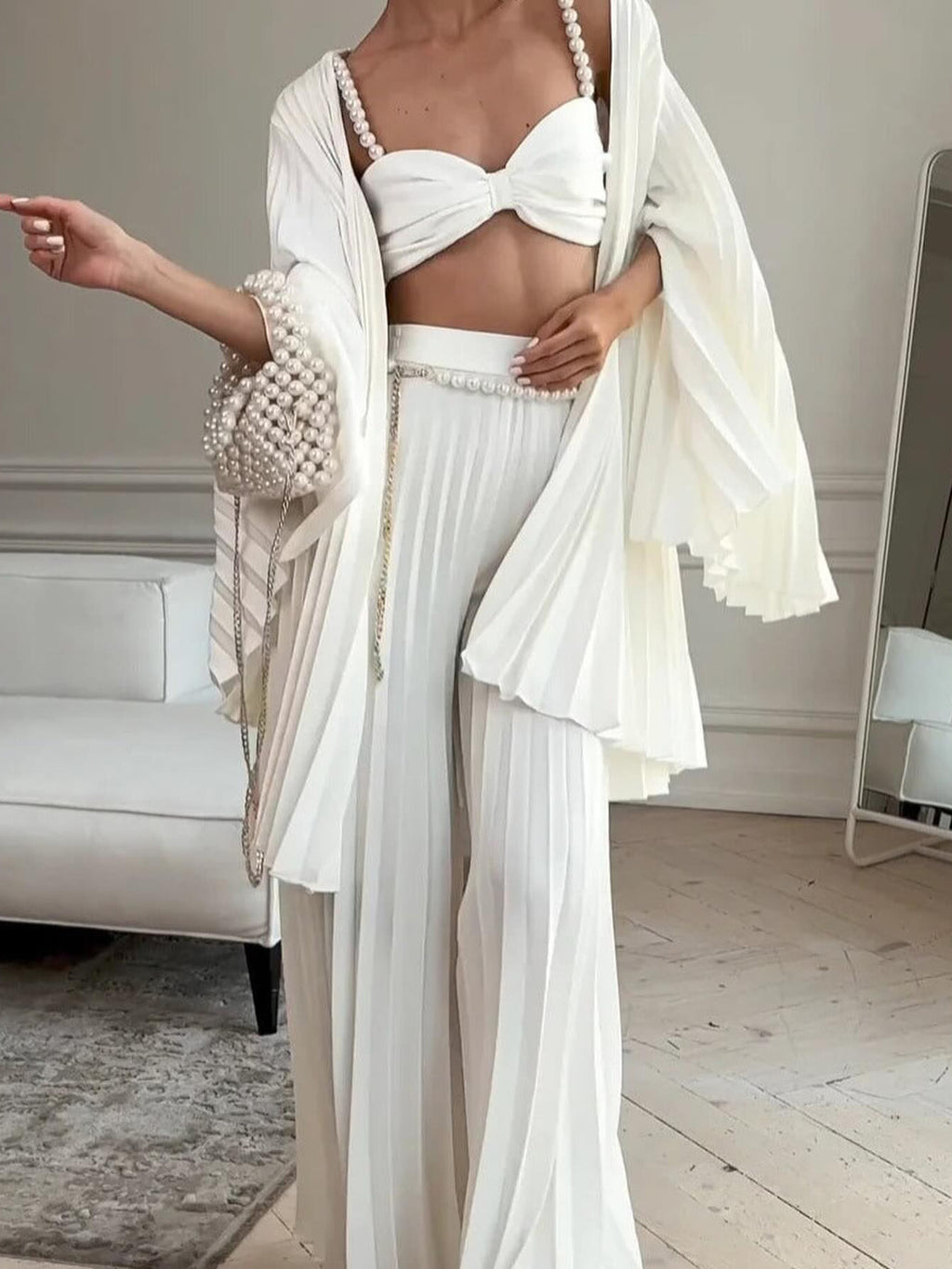 Model wearing a white bow-front crop top, pleated open cardigan and wide-leg trousers