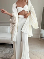 Model wearing a white bow-front crop top, pleated open cardigan and wide-leg trousers