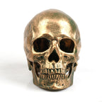 Gold-colour skull decoration viewed from the front, with dark eye and nose openings and visible sculpted teeth.