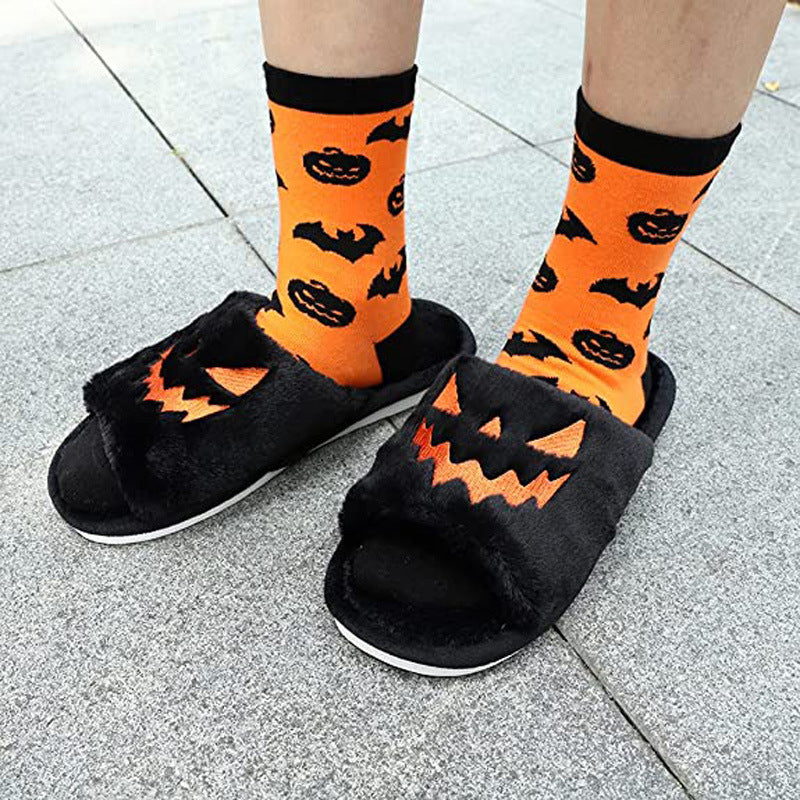 Black open-toe pumpkin-face slide slippers with orange facial details, worn with orange Halloween socks.