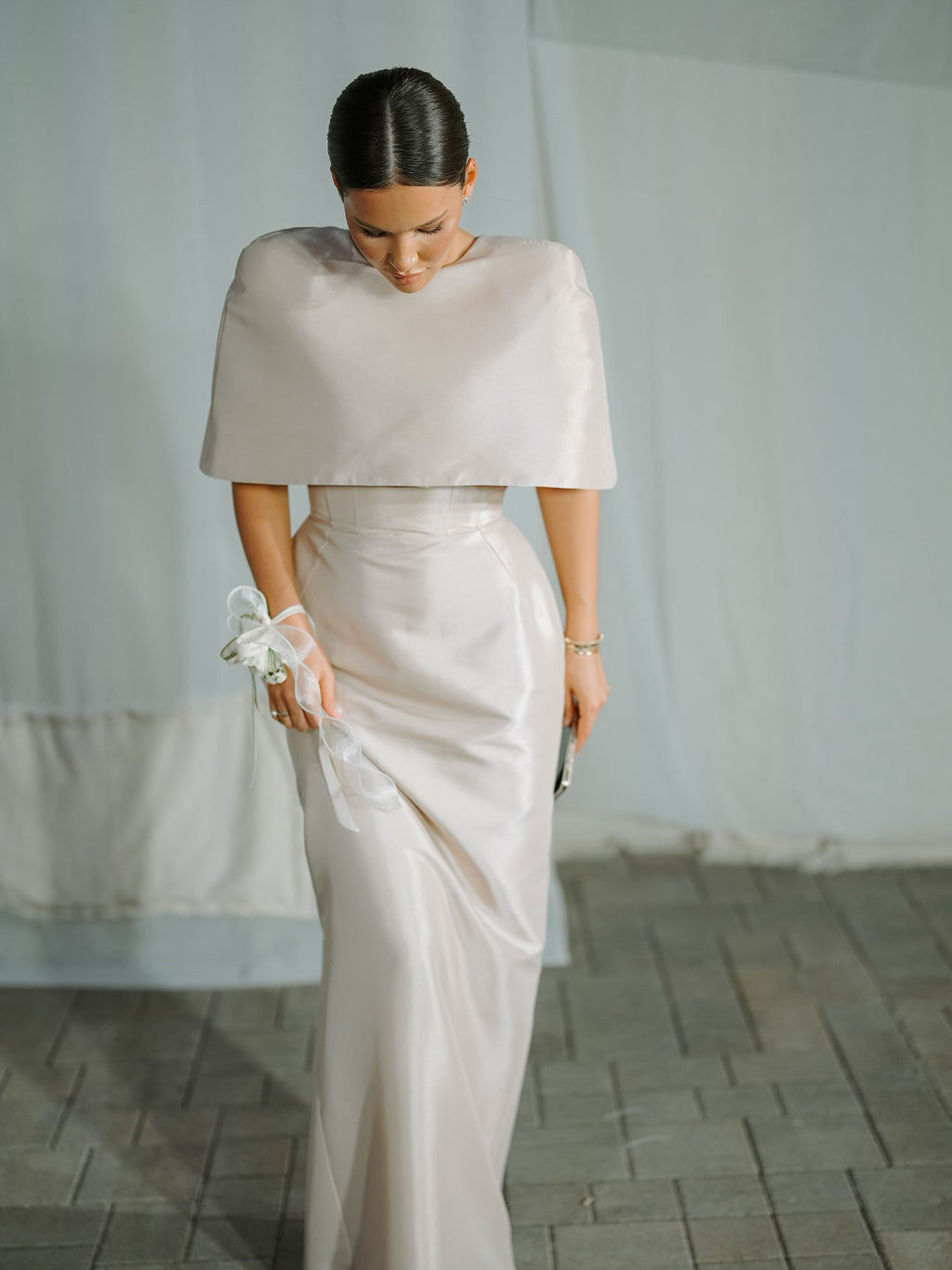 Pale cape-overlay fitted dress worn by a model in front of a neutral curtain