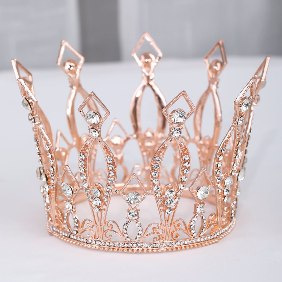Rose-gold-tone occasion crown with clear decorative stones on a light background.