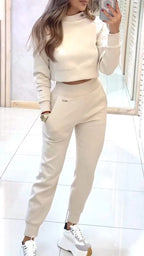 Model wearing an ivory cropped sweatshirt and matching joggers in a pale tiled interior