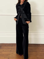 Model wearing a black bow-front jacket and wide-leg trousers, shown from the front