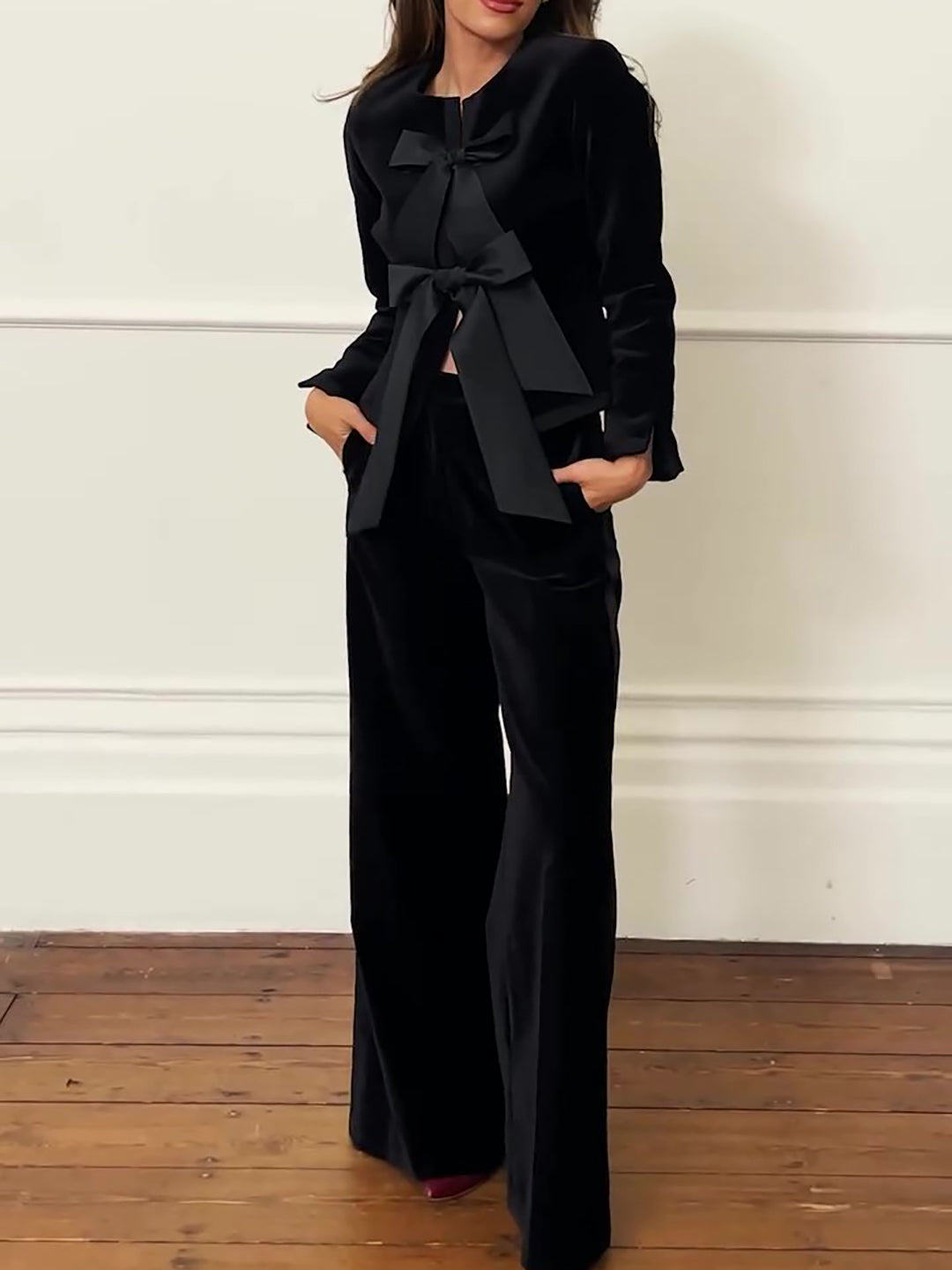 Model wearing a black bow-front jacket and wide-leg trousers, shown from the front
