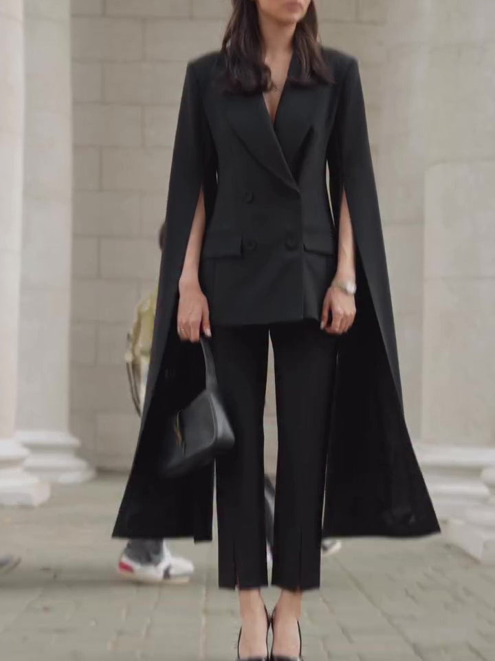 Model wearing a black double-breasted cape blazer with slit arm openings and cropped black trousers