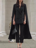 Model wearing a black double-breasted cape blazer with slit arm openings and cropped black trousers