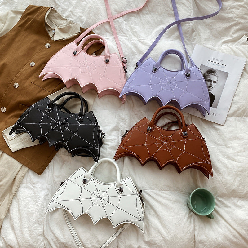 Black, white, brown, pink and lavender bat-wing-shaped bags displayed as separate colour options on a bed.