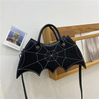 Black bat-wing-shaped bag hanging on a wooden chair by its handles.
