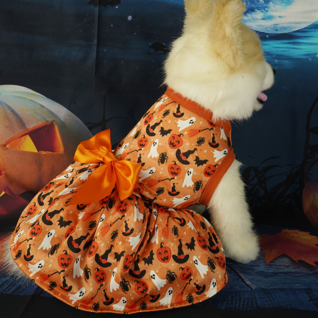 Orange pet dress with pumpkin, ghost and witch-hat print and a large orange bow, displayed on a plush dog