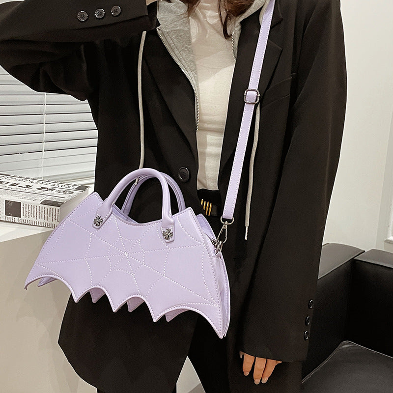 Lavender bat-wing-shaped crossbody bag worn at the hip over a dark coat.