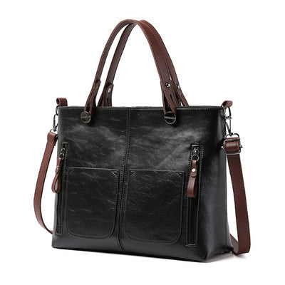 Black two-handle shoulder bag with front pockets, vertical zippers and a long strap on white.
