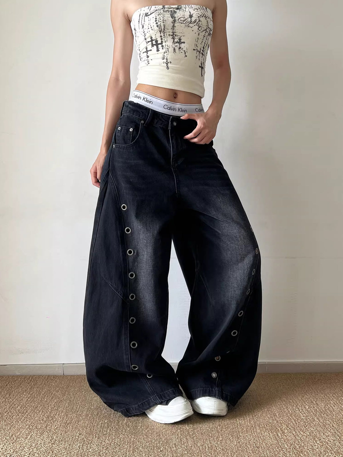 Model wearing washed black curved-leg jeans with metal eyelet rows and front pockets