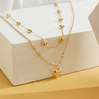 Gold-tone double-layer heart necklace displayed over a white block on a yellow surface.