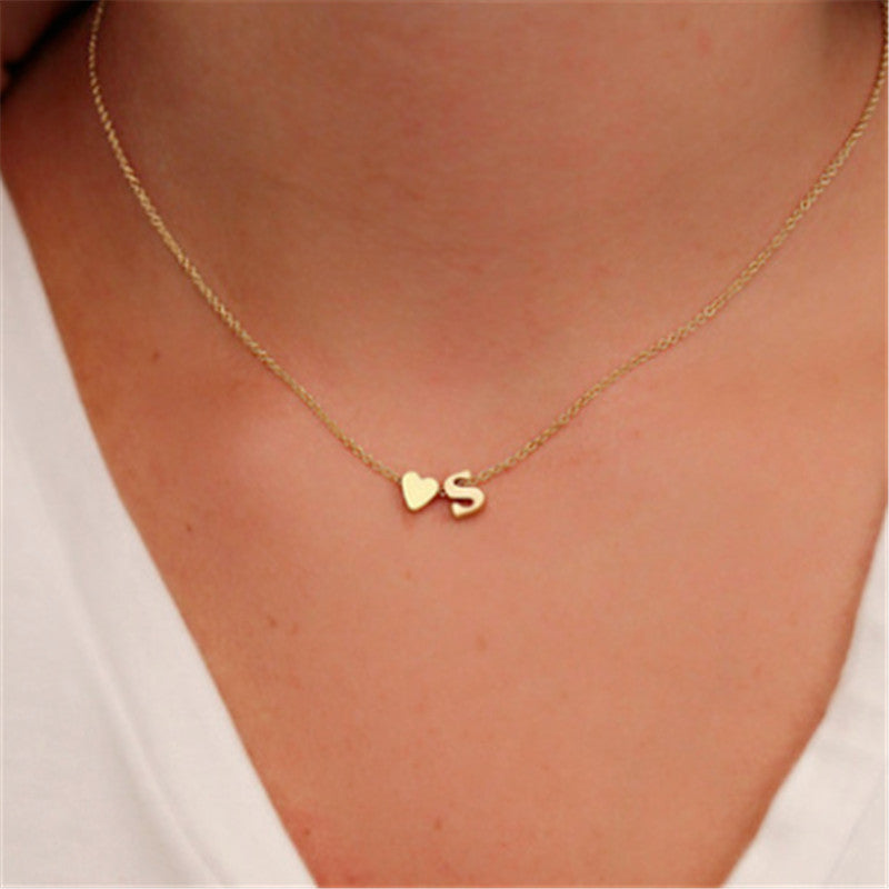 Gold-colour S initial and small heart necklace, shown worn with a white V-neck top.