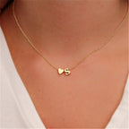 Gold-colour S initial and small heart necklace, shown worn with a white V-neck top.