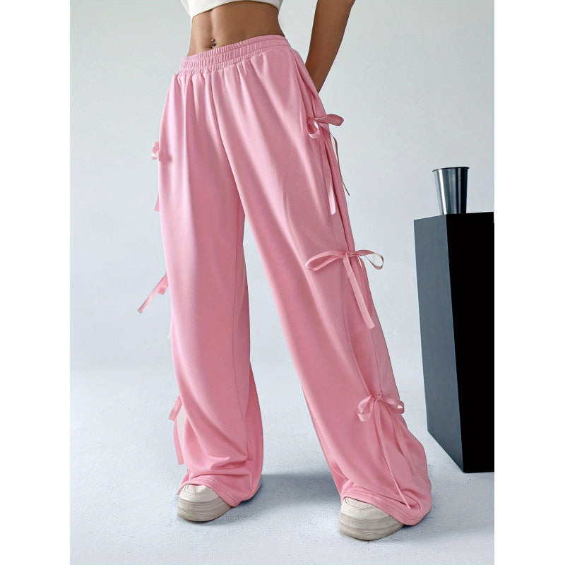 Pink wide-leg trousers with an elasticated waist and ribbon bows along the outer legs, shown on a model.