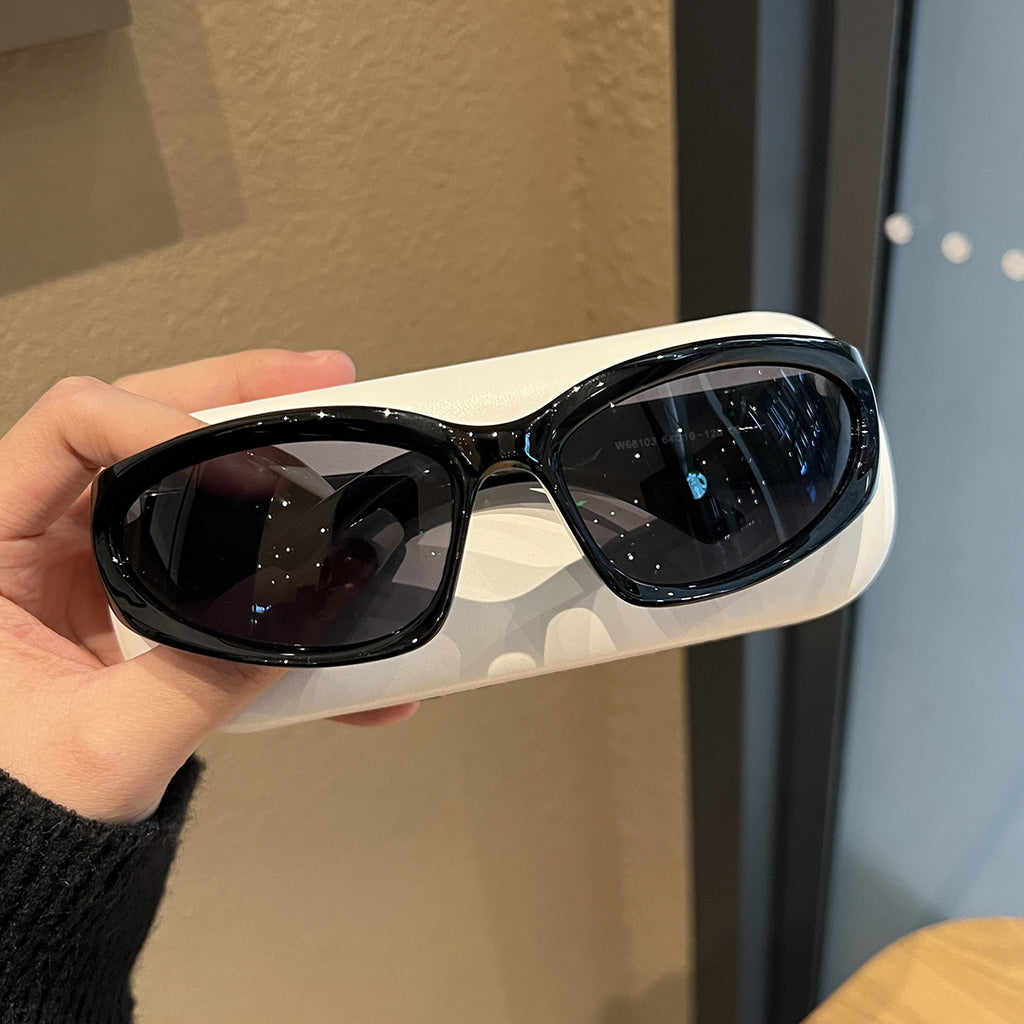 Hand holding one pair of black oval wraparound sunglasses on a white display box