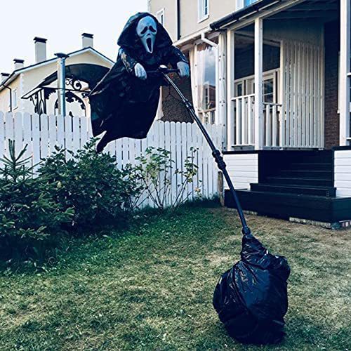 Black hooded scarecrow decoration with a white mask displayed on a support pole in a front yard.