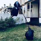 Black hooded scarecrow decoration with a white mask displayed on a support pole in a front yard.
