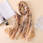 Khaki scarf with a flowering branch print arranged on a pale surface