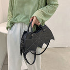Black bat-wing-shaped bag held at the side, showing its shoulder strap and spider-web stitching.