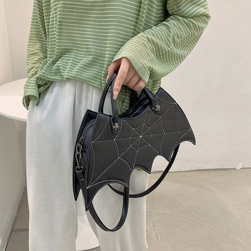 Black bat-wing-shaped bag held at the side, showing its shoulder strap and spider-web stitching.