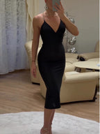 Full front view of a black V-neck midi dress with thin rhinestone straps, worn indoors