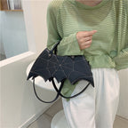 Black bat-wing-shaped bag held by its handles in front of a green striped top.