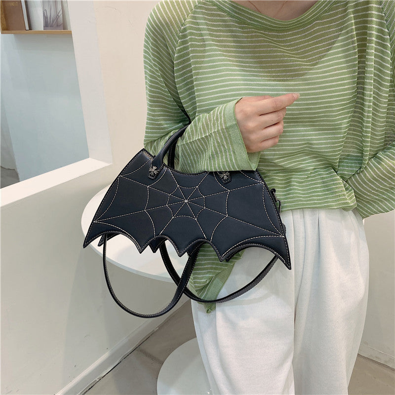Black bat-wing-shaped bag held by its handles in front of a green striped top.