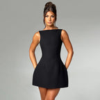 Black sleeveless mini dress with a high neckline and flared skirt, worn against a gray studio background.